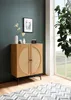 A modern sideboard with rattan detailing is placed in a room with a dark teal wall and a large window. A rug with a geometric pattern is on the floor in front of the sideboard. Produktbild-Vorschau
