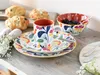 A colorful floral patterned dinnerware set with a mug, plate, and bowl, along with some pastries and blueberries, arranged on a wooden table. Náhľad obrázku produktu