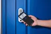 A hand holding a smartphone near a smart door lock on a blue door. Anteprima dell’immagine prodotto