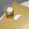 A jar of cream and a dollop of cream on a gold surface. Produktbild-Vorschau
