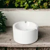 A white ashtray sits on a stone ledge with green foliage in the background. Anteprima dell’immagine prodotto