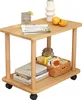 A small wooden side table with two shelves, decorated with a glass of drink, oranges, a vase, books, and a basket of items. Produktbild-Vorschau