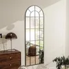 A tall, arched mirror with a grid pattern is shown leaning against a wall in a room, reflecting a bed and blinds. Produktbild-Vorschau