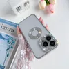 A hand holding a clear iPhone 13 Pro Max case with silver trim and diamond accents, placed on a white surface with a book and flowers in the background. Produktbild-Vorschau