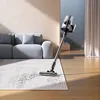 A cordless vacuum cleaner is shown in a modern living room, cleaning a rug in front of a sofa. Produktbild-Vorschau