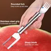 A hand is holding a stainless steel watermelon slicer and fork tool over a sliced watermelon. Produktbild-Vorschau