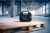A blue and black Bosch radio sits on a wooden pallet in a large, unfinished industrial building. Produktbild-Vorschau