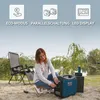 A woman is operating a portable generator outdoors near a body of water, with camping chairs in the background. Podgląd zdjęcia produktu