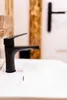 A black faucet is shown in a bathroom sink. Náhled obrázku produktu