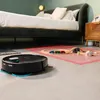 A robot vacuum cleaner is cleaning the floor next to a bed and a toy train track. Produktbild-Vorschau