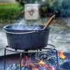 A Dutch oven is being heated over a campfire with a wooden spoon inside. Produktbild-Vorschau
