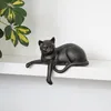 A dark-colored cat figurine is lying on a white shelf, with a green and yellow leafed plant to the left. Anteprima dell’immagine prodotto