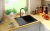 A kitchen sink area with a black granite sink, faucet, plants, and food items on a wooden countertop. Produktbild-Vorschau