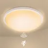A white, round LED ceiling light with a warm yellow glow, mounted on a light beige ceiling. Two white icons are displayed below the light: one representing motion detection (concentric arcs) and the other a running person. Náhľad obrázku produktu