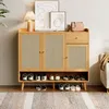 A wooden shoe cabinet with rattan doors and a drawer, filled with shoes and decorated with artwork and a lamp. Voir les images du produit