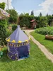 A child's play tent shaped like a castle is set up on a grassy lawn in a garden, with a brick pathway and trees in the background. Produktbild-Vorschau