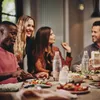 A group of friends enjoying a meal together at a table, with bottles of sparkling water and food laid out. Produktbild-Vorschau