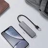 A USB hub is shown next to a smartphone and a wallet, with a bag in the background. Produktbild-Vorschau