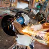 A person is using a Scheppach double grinder to sharpen a tool, with sparks flying. Produktbild-Vorschau