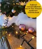 A close-up of a Christmas tree branch with lights and ornaments, suggesting festive decoration. Produktbild-Vorschau