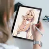 A person is using a stylus to draw on a tablet, which displays a digital illustration of a woman holding a baby. The scene is set on a desk with a phone and glasses in the background. Anteprima dell’immagine prodotto