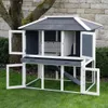 A rabbit hutch is shown outdoors on a grassy lawn, with a stone wall and tree in the background. Voir les images du produit