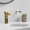 A modern bathroom sink with a brass waterfall faucet, a glass toothbrush holder, and a small potted succulent. Podgląd zdjęcia produktu