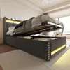 A modern upholstered bed frame with its storage compartment open, revealing stored items. The bed features LED lighting and a headboard with a shelf and USB ports.