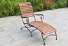 A wooden and metal chaise lounge is placed on a paved patio next to a garden. Produktbild-Vorschau