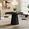 A modern dining room with a round black table and chairs, artwork on the wall, and a large window. Produktbild-Vorschau