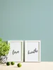 Two framed pictures with inspirational quotes and a potted plant on a wooden surface against a blue textured wall. Produktbild-Vorschau