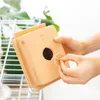 A person's hands are holding a peach-colored money box with a hole in the front, and a toothpick is being inserted into a small circular opening on the side. Produktbild-Vorschau