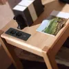 A black power strip with two USB ports is embedded in a wooden table, next to a magazine and a decorative object. Produktbild-Vorschau