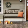 A bronze metal garden bench with a decorative backrest featuring birds and branches, placed on a patio with pumpkins and a wreath on the wall. Produktbild-Vorschau