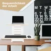 A standing desk converter with a laptop, keyboard, and mouse on a wooden desk, with a calendar and plant in the background. Produktbild-Vorschau