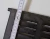 A close-up of a cast iron grate with a ruler measuring its width. Voir les images du produit