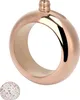 A rose gold colored flask shaped like a bracelet with a decorative cap next to it. Podgląd zdjęcia produktu
