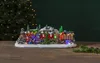 A festive LED light-up Christmas village scene with a train, houses, trees, and people, set against a dark green background with bokeh lights. Podgląd zdjęcia produktu