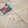 A close-up of a cream-colored ribbed blanket with a book and a perfume bottle on it. Podgląd zdjęcia produktu