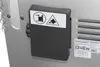 Close-up of a small black electrical box with warning labels attached to the side of a metal appliance. Produktbild-Vorschau