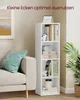 A tall, narrow white bookshelf filled with books and decorative items, placed next to a beige sofa in a living room setting. Produktbild-Vorschau