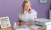 A woman is using a Brother sublimation printer to print designs onto fabric, with a framed picture and a mug on the desk. Náhled obrázku produktu