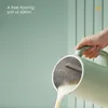 A hand is pouring a light-colored liquid from a green pitcher into an unseen container against a light green background with vertical paneling. Anteprima dell’immagine prodotto