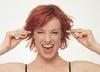 A woman with red hair is holding earplugs to her ears. Produktbild-Vorschau