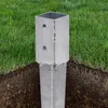 A metal post anchor is partially buried in the ground, with green grass surrounding it. Produktbild-Vorschau