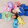 Two young girls and a young woman lying on the floor surrounded by Care Bear plush toys. Anteprima dell’immagine prodotto