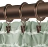 A close-up view of curtain rings and clips holding up a green curtain. Podgląd zdjęcia produktu