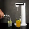 A hand is pouring sparkling water from a bottle into a glass with lime slices, next to a glass of yellow drink with a straw and a white soda maker. Podgląd zdjęcia produktu