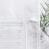 A close-up view of a white sheer curtain with text printed on it, and a plant in the background. Produktbild-Vorschau
