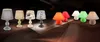 A collection of various table lamps displayed on a reflective surface against a dark background. Produktbild-Vorschau